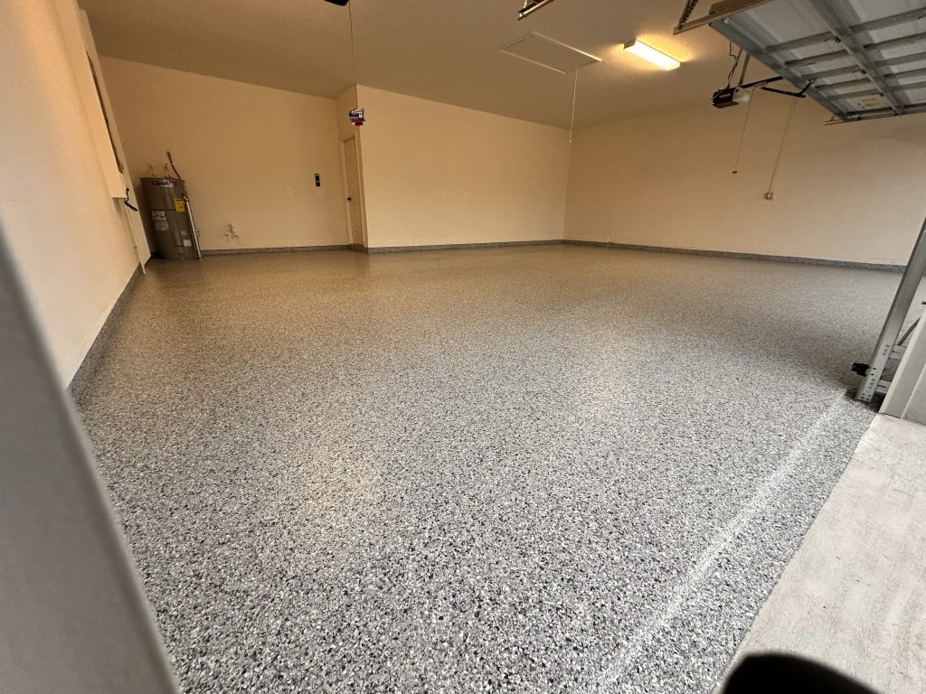 Freshly coated epoxy garage floor with light gray and black flake finish, open garage door visible.